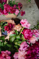 a beautiful and gentle young woman lies in peony flowers. feminine beauty. 