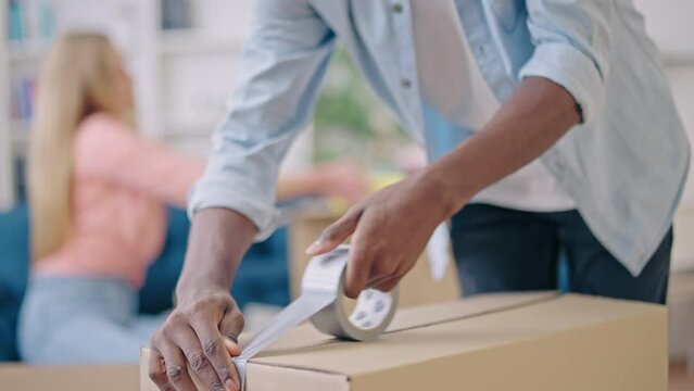 Black man taping boxes, couple packing belongings, moving into a new apartment