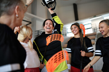 Obraz premium Group of young and old cheerful women, floorball team players, in gym cebrating victory.