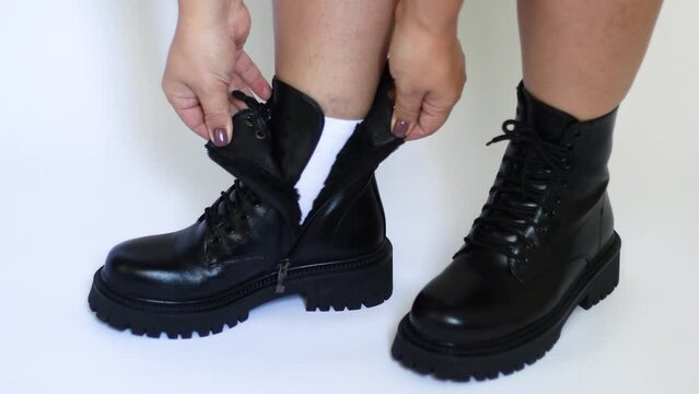 Cropped Photo Of Woman Wearing, Putting On Black Boots With Shoelace, Unzipping Shoes, Showing White Sock On White Background. Advertisement, Unisexual Fashion, Shoes For Women. Close-up. Studio Shot.