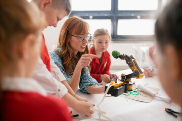 Group of kids with young science teacher programming electric toys and robots at robotics classroom