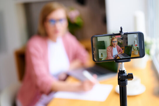 Selective focus of woman blogger broadcasts live on phone at home next to laptop