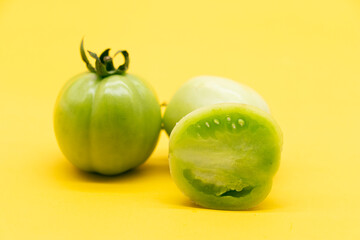 Whole and halved fresh green unripe tomatoes isolated on yellow background
