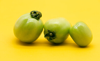 Fresh green unripe tomatoes isolated on yellow background.