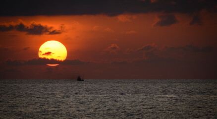 Isolated small fishing boat and the golden sunset, the fishing boat sails as the sun sets behind the clouds and the horizon. Scenic seascape photograph.