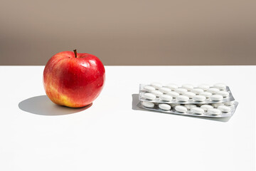 Red apple and pills or vitamin capsules on white table, copy space. Wellness, diet or supports for health concept.