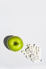 Green apple and pills or vitamin capsules on white table, copy space. Wellness, diet or supports for health concept.