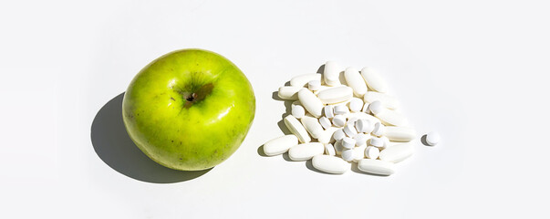 Green apple and pills or vitamin capsules on white table, copy space. Wellness, diet or supports for health concept.