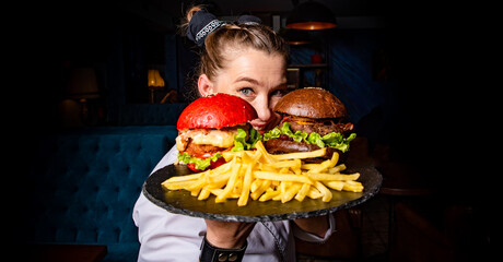 woman chef with two burger on dark background in cafe