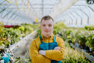 Young employee with Down syndrome working in garden centre, looking at camera with arms crossed.