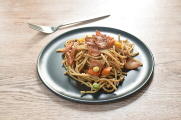 fried spaghetti black pepper sauce topping crispy bacon and corn with green pea on plate 