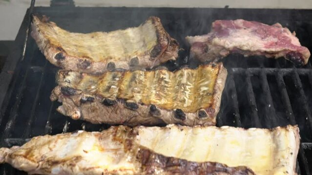 Slowmotion of chef cooking tasty ribs pork on a barbecue grill. Close up of delicious grilled pig cooked in BBQ of garden home at holiday vacations in Spain.