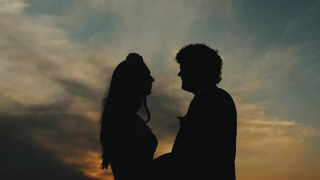 Silhouette of loving couple holding each other hands and walking on the beach during sunset slow motion.