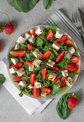Healthy salad with strawberries, spinach, feta and pine nuts dressed with balsamic in plate on gray background