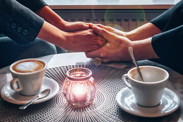 clasped hands of a loving couple over a table in a cafe with two symbolic cups of coffee. For him - empty, everything is decided, for her untouched, there are doubts