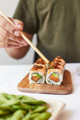 Comiendo con palillos aburi uramaki. Sushi roll de salmón y aguacate con cebolla caramelizada.
