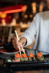 Comiendo uramaki de tempura de salmón en un restaurante japonés. Cogiendo con palillos sushi 