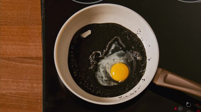 male hands break an egg into a frying pan in black oil. fried eggs in black oil, similar to unfiltered petroleum products. boiling dark oil frame from above 2.8k top shot