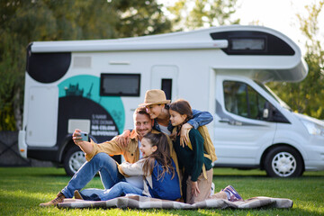 Happy young family with two children ltaking selfie with caravan at background outdoors.