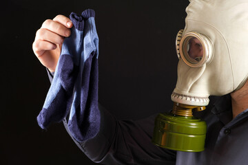 A man in a gas mask holds dirty smelly socks. The problem of unpleasant foot odor in men