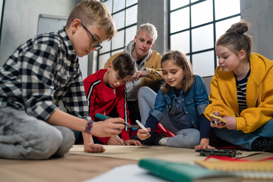 Group of happy kids with their teacher working on project together at classroom.