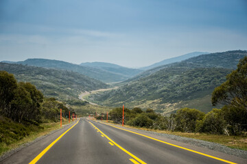 Open empty road surrounded by the mountains. Mountain winging road with high visible yellow lines. Snowy Mountains, New South Wales, Australia