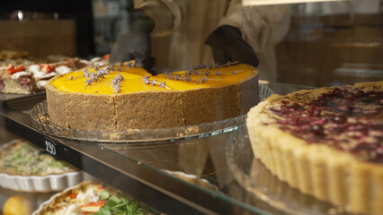 Pastry cook puts plate with cheesecake on showcase in cafe. Cheesecake with orange jam decorated with lavender flowers stands on showcase