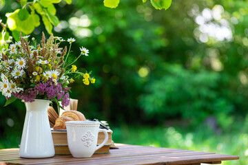 Bouquet of meadow flowers, croissant, cup of tea or coffee, books on table in summer garden. Rest in garden, reading books, breakfast, vacations in nature concept. Summertime in garden on backyard