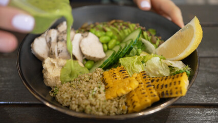 Bowl with avocado and turkey meat seasoned with guacamole salsa. Female hands in restaurant pour guacamole salsa sauce into dish closeup