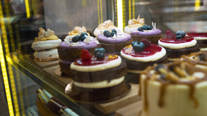 Cakes assortment in cafe showcase. Variety of beautiful desserts on shelf behind showcase glass. Pastry with different decorations and taste closeup