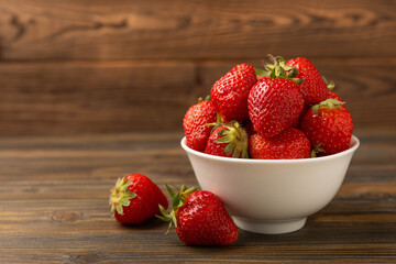Fresh ripe juicy strawberries in a bowl on a brown wooden table. Summer background composition with strawberries. Fruit concept.Vitamins.Eco berries. Copy space