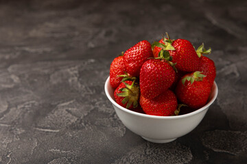 Fresh ripe juicy strawberries in a bowl on a black cement table. Summer background composition with strawberries. Fruit concept.Vitamins.Eco berries. Copy space