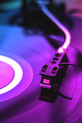 DJ turntable playing a vinyl record. Close up of needle. Blue and pink lighting. Music party...