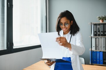 Portrait Of Female Doctor Wearing White Coat In Office.