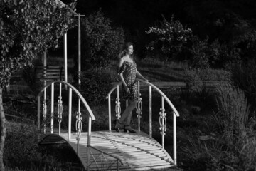 Obraz premium Beautiful slender woman in dress standing on a small bridge in black and white