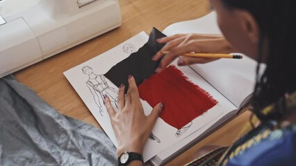 Close up shot of female designer placing two pieces of fabric on fashion sketch while working on new garment collection - Powered by Adobe