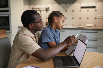 Fototapeta na wymiar Side view portrait of caring black father helping daughter with homework in cozy scene, copy space