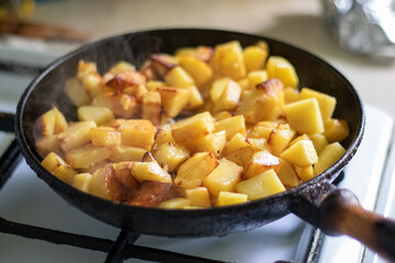 Roasting fresh potatoes in a cast iron skillet with sunflower oil. A view of a stovetop with a frying pan filled with golden fried potatoes in a real kitchen. Food cooked in a homemade frying pan.