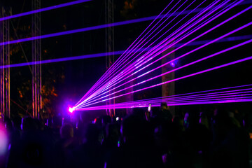 Purple laser neon beams. Crowd of people watching laser show at street festival. Many people enjoy the concert.