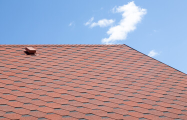 New roof with red shingles against the blue sky. High quality photo. Tiles on the roof of the house. Use to advertise roof fabrication and maintenance. Spotted texture. Affordable roofing.