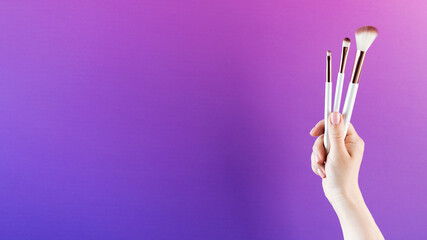 Cosmetic brush set in a female hand on a purple and pink background. Copy space.