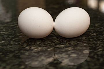 Two white chicken eggs on a granite counter with a shallow depth of field and copy space