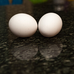 Two white chicken eggs on a granite counter with a shallow depth of field and copy space
