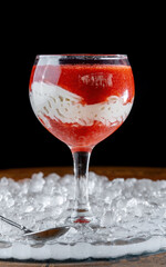 Dessert with berry puree, strawberries and whipped cream in a glass, side view.
