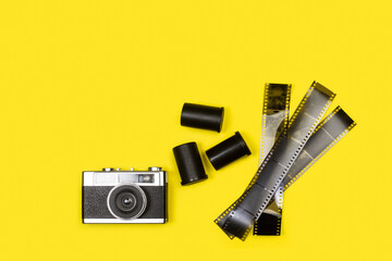 Cámara de foto analógica con carretes y negativos sobre un fondo amarillo brillante liso y...