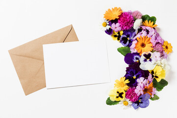 Festive card with envelope template. Spring and summer colorful flowers and blank paper sheet card mockup on white background. Flat lay, copy space for text, top view. Round frame wreath pattern.