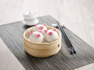 Steamed Custard Bun with Pine Seeds in Piggy Shape served in a wooden bowl with chopsticks isolated on mat side view on grey marble background