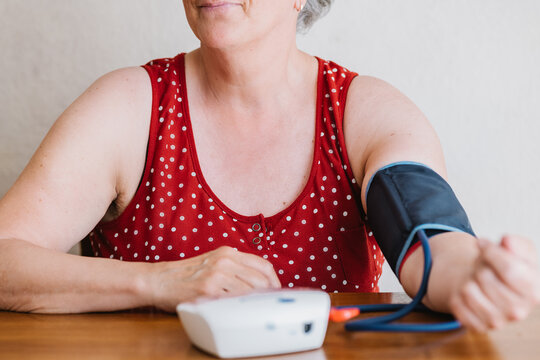 Anonymous elderly woman measuring blood pressure with electronic device at home