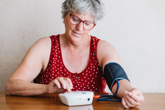 Elderly woman measuring blood pressure with electronic device at home