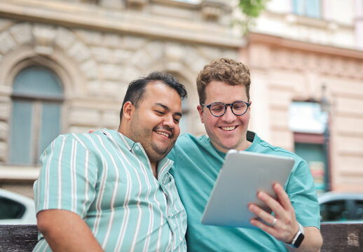 two men hug each other on a bench and use a tablet